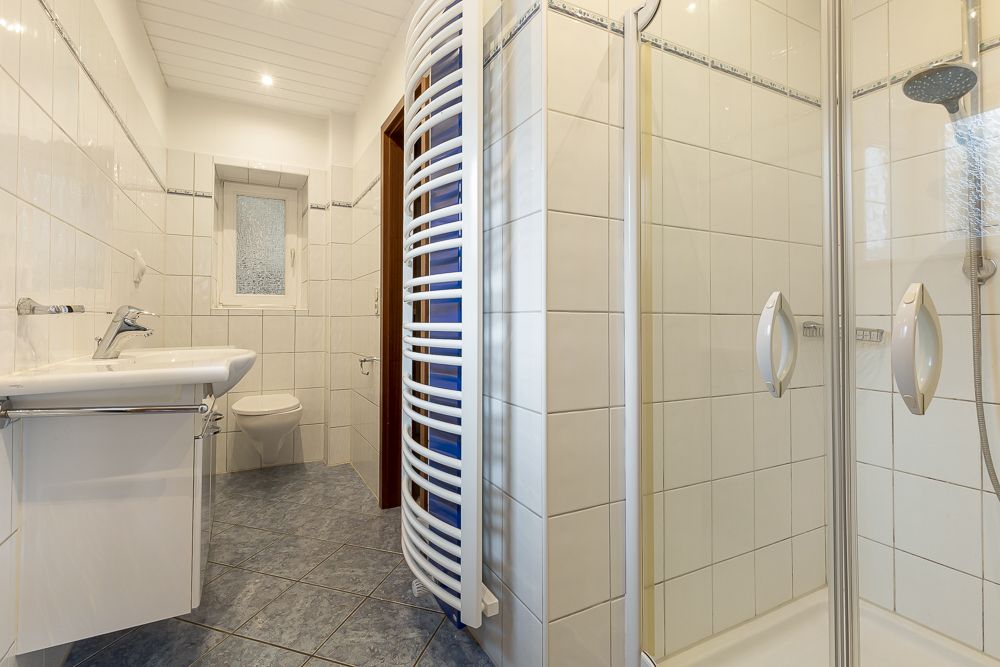 Modernes Badezimmer mit Dusche, Waschbecken, WC, Fenster und Handtuchheizkörper.