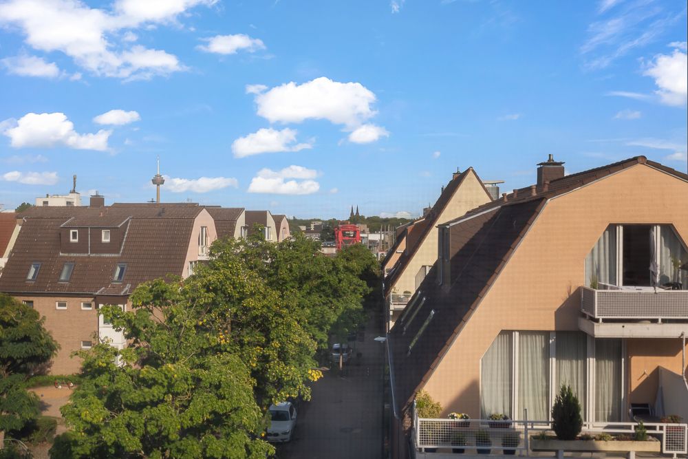 Blick auf Wohnhäuser mit Satteldächern und Balkonen an einer ruhigen Straße, Bäume im Vordergrund.