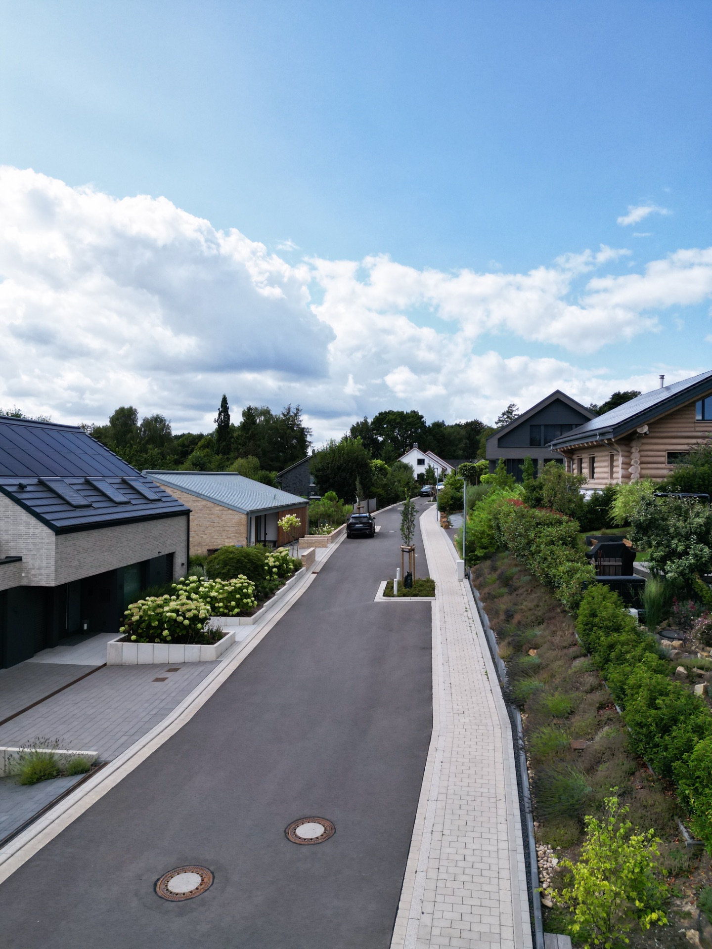 Moderne Wohnstraße mit Häusern, Gärten und geparktem Auto an einem sonnigen Tag.
