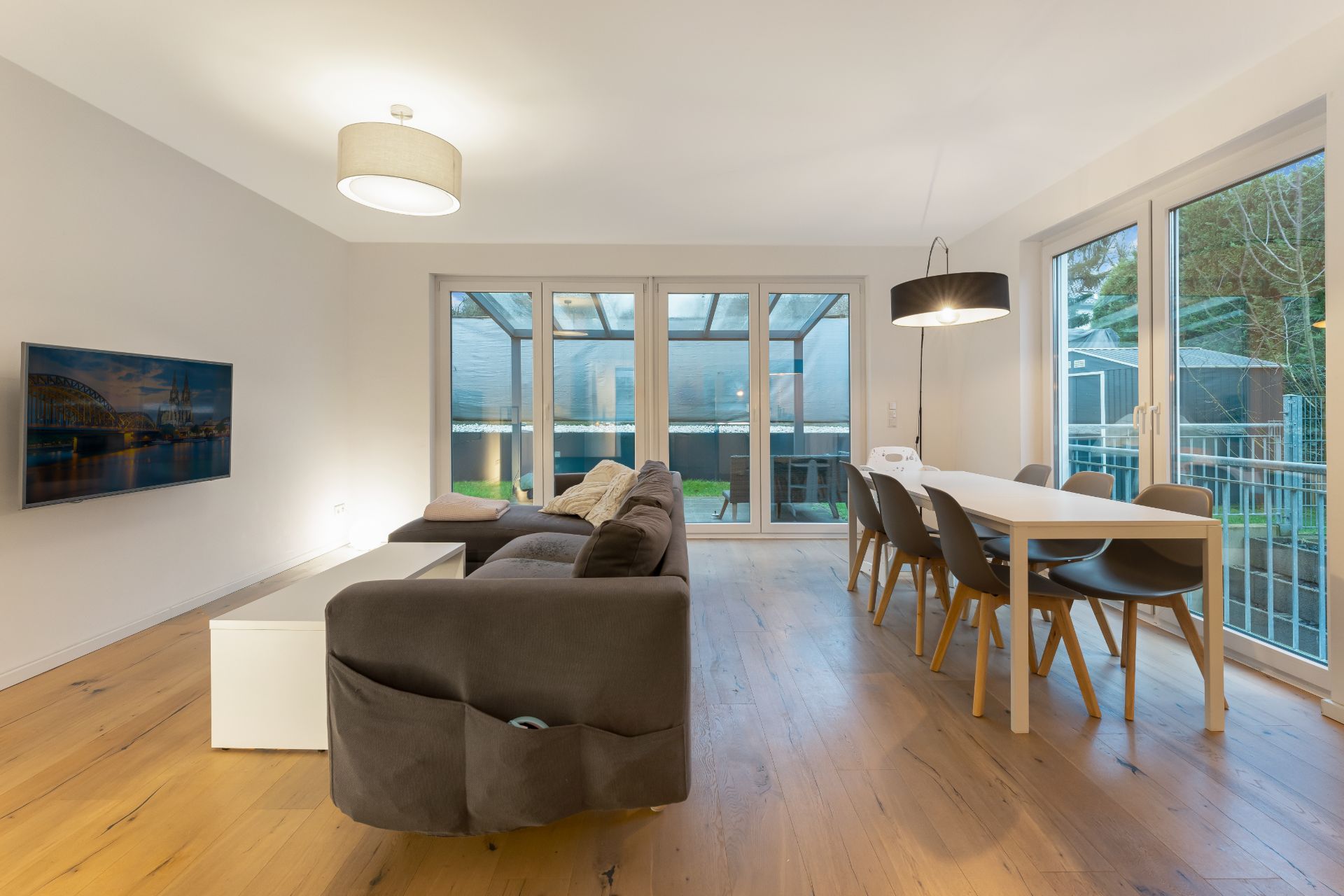 Wohnzimmer mit Sofa, Esstisch, Stühlen und großen Fenstern zu einer Terrasse.