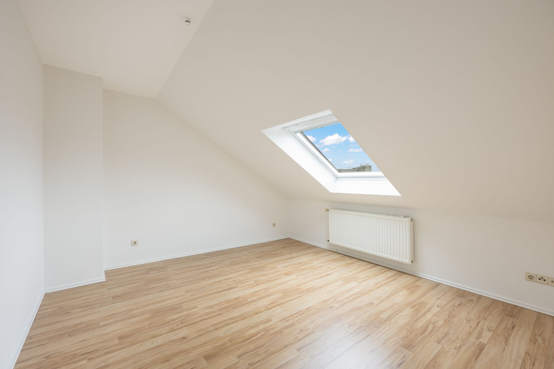 Helles Zimmer mit Dachschräge, Laminatboden, Fenster und Heizkörper.