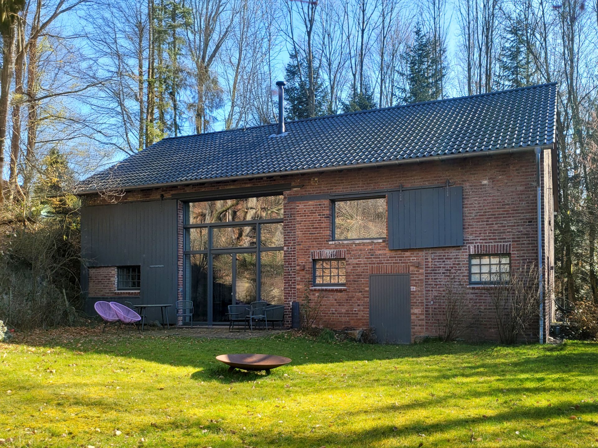 Backsteinwohnhaus mit Schrägdach, großen Fenstern und Garten im Vordergrund.