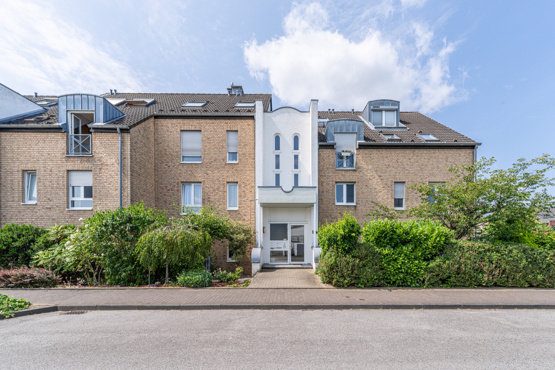 Mehrfamilienhaus mit Klinkerfassade und gepflegtem Eingangsbereich, umgeben von Grünpflanzen.