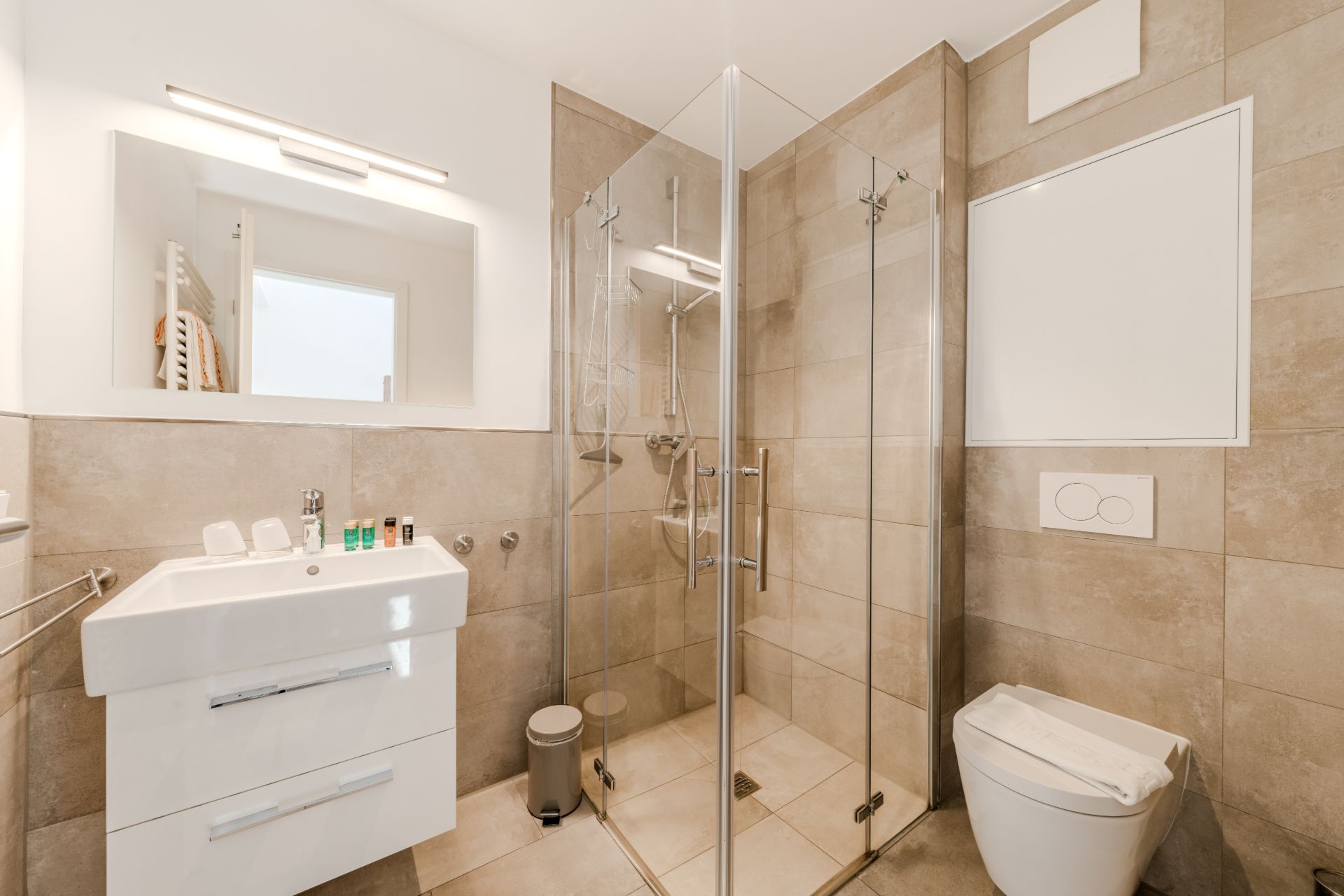 Modernes Bad mit Glasdusche, Waschbecken, Spiegel und WC, helle Fliesen an Wand und Boden.