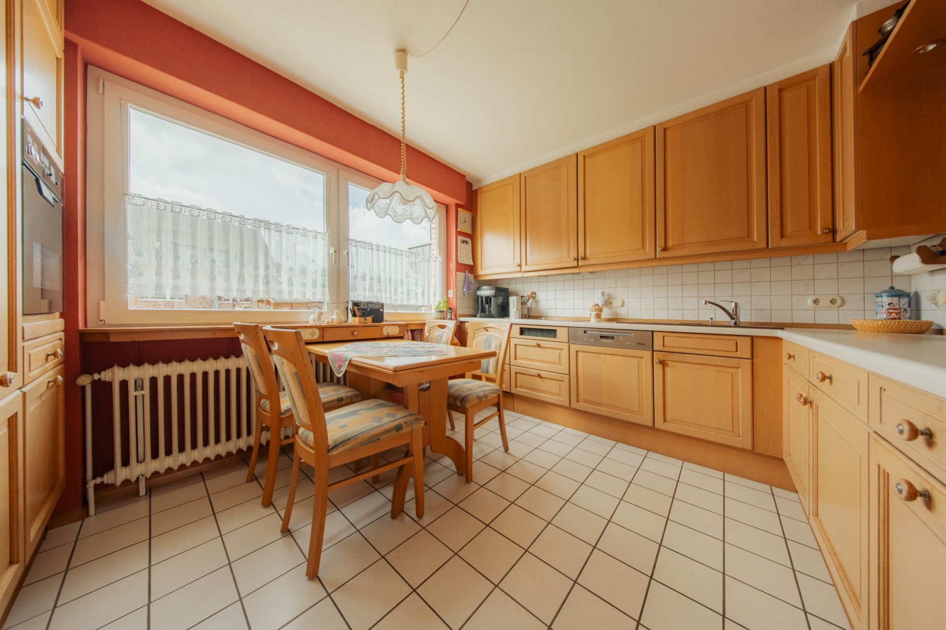 Helle Küche mit Holzmöbeln, Esstisch und vier Stühlen vor einem großen Fenster.