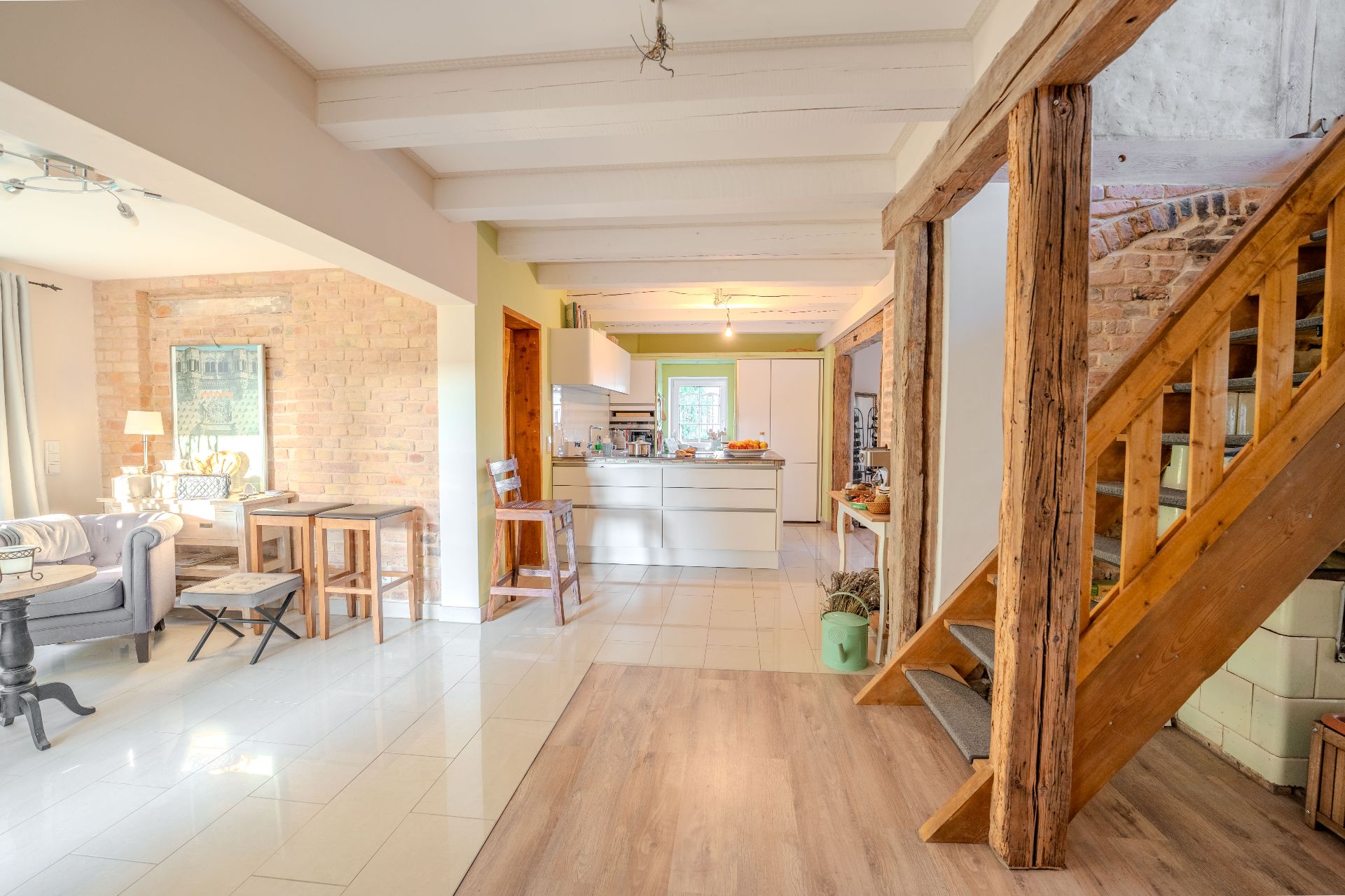 Heller Wohnraum mit Sofa, Esstisch, moderner Küche und Holztreppe.