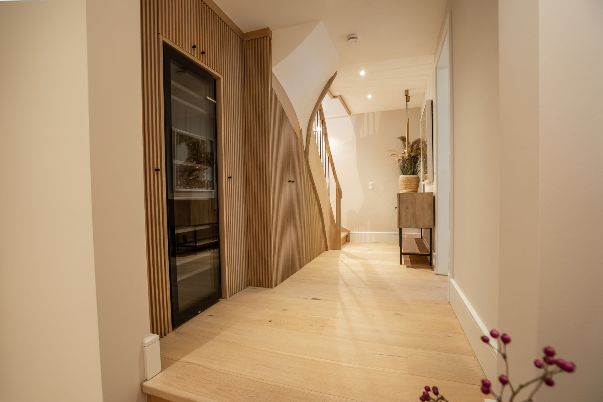Heller Flur mit Holzfußboden, Treppe, Schrank und einer kleinen Kommode mit Pflanze.