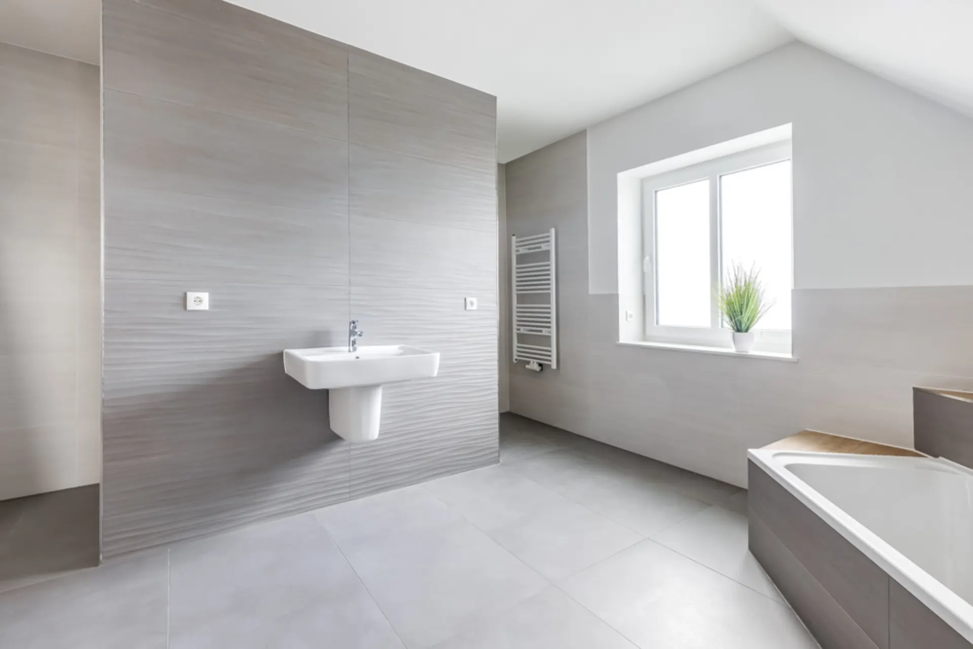 Modernes, helles Badezimmer mit Waschbecken, Badewanne, Fenster und Handtuchheizkörper.