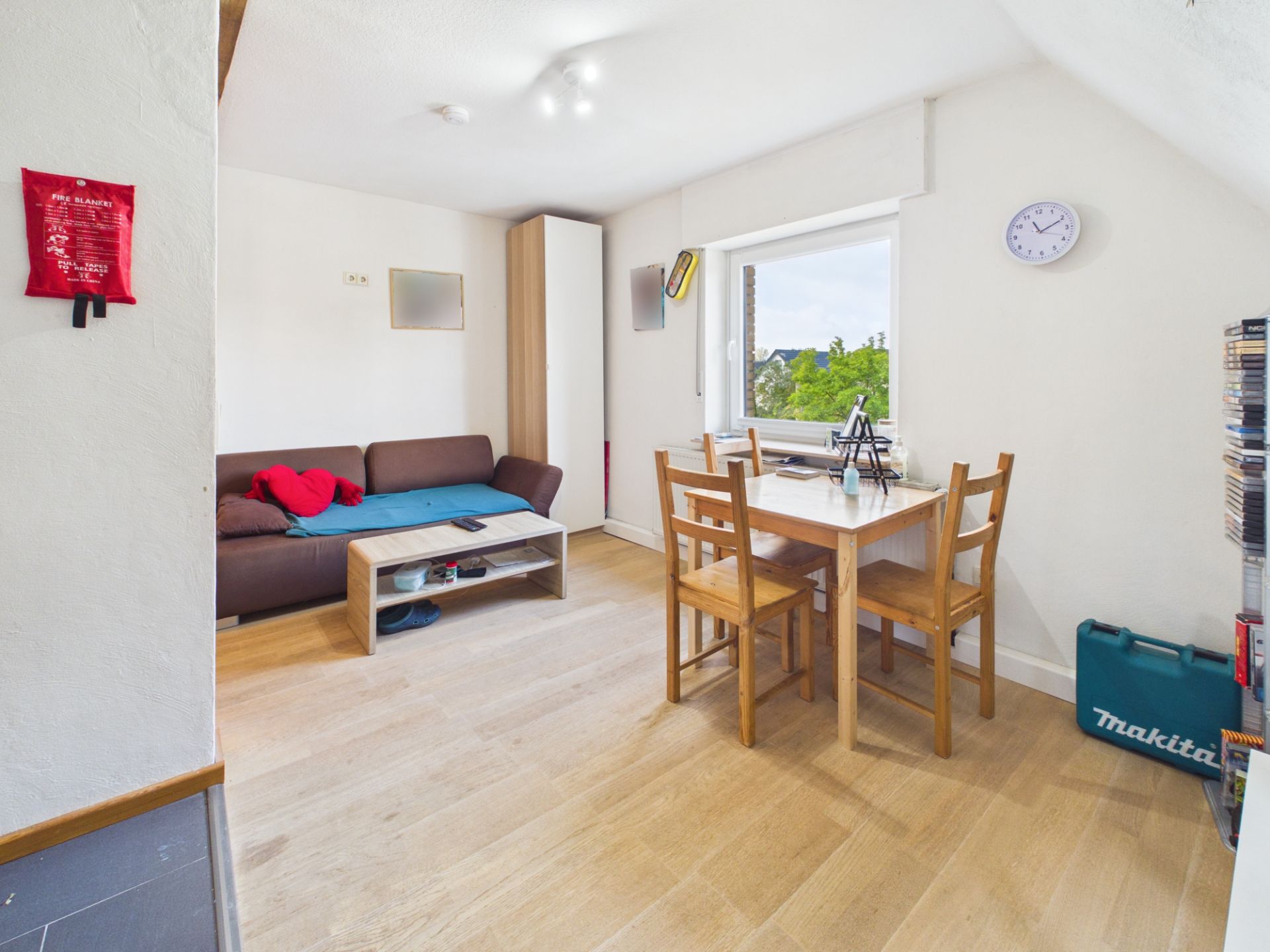 Helles Wohnzimmer mit Sofa, Holztisch, vier Stühlen und großem Fenster.