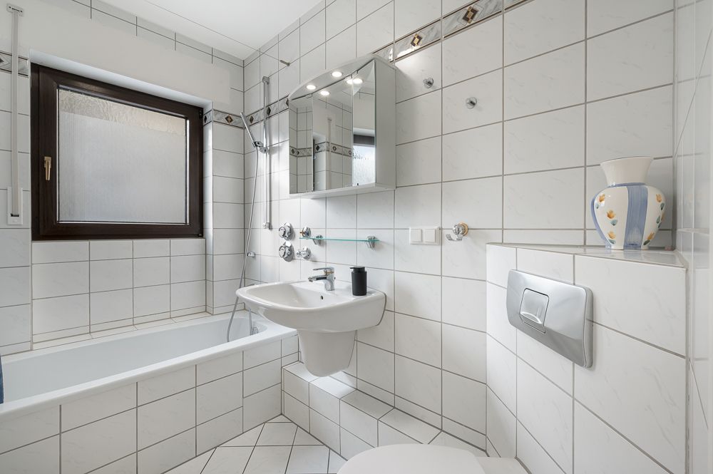 Helles Badezimmer mit Badewanne, Waschbecken, Spiegel, Fenster und WC.