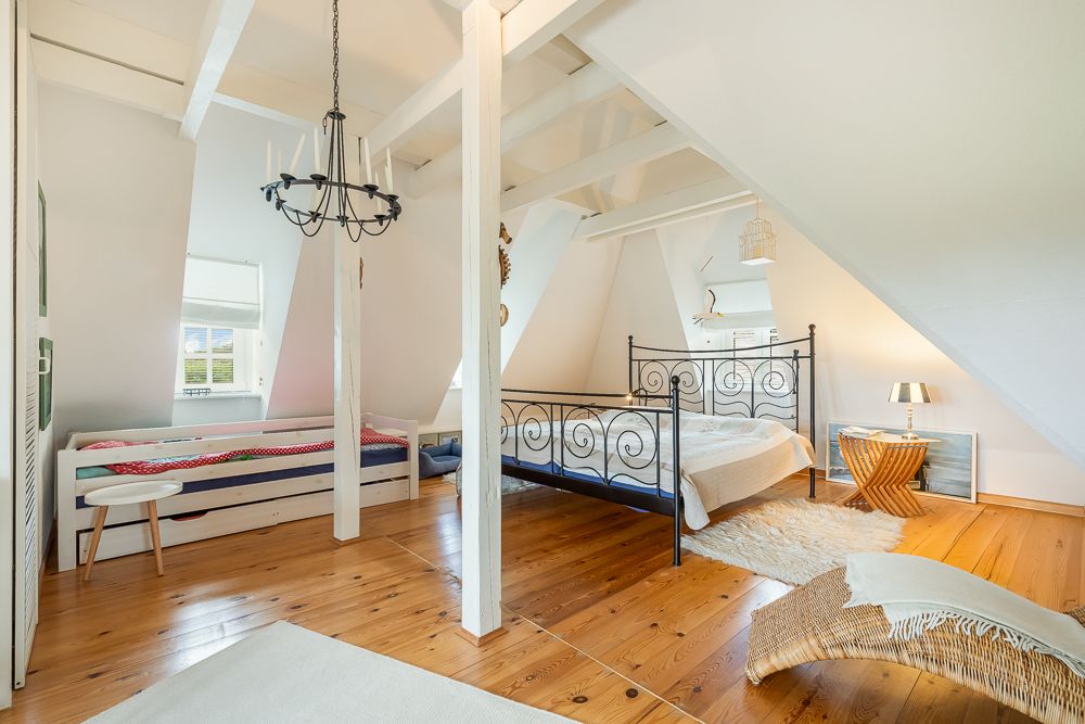 Helles Schlafzimmer mit Metallbett, Einzelbett, Holzboden und sichtbaren Dachbalken.