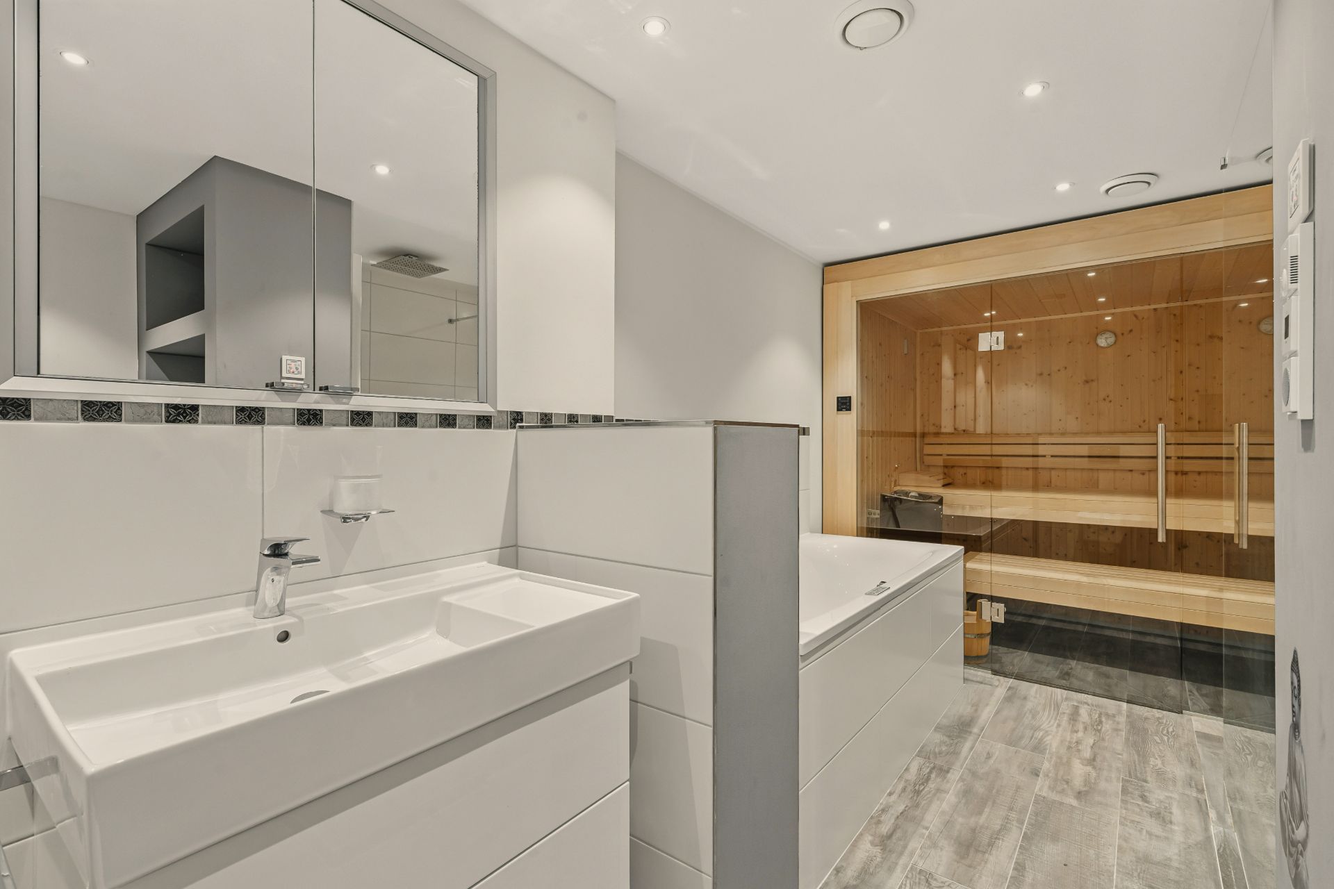 Modernes Badezimmer mit Waschbecken, Badewanne und einer Holzsauna im Hintergrund.