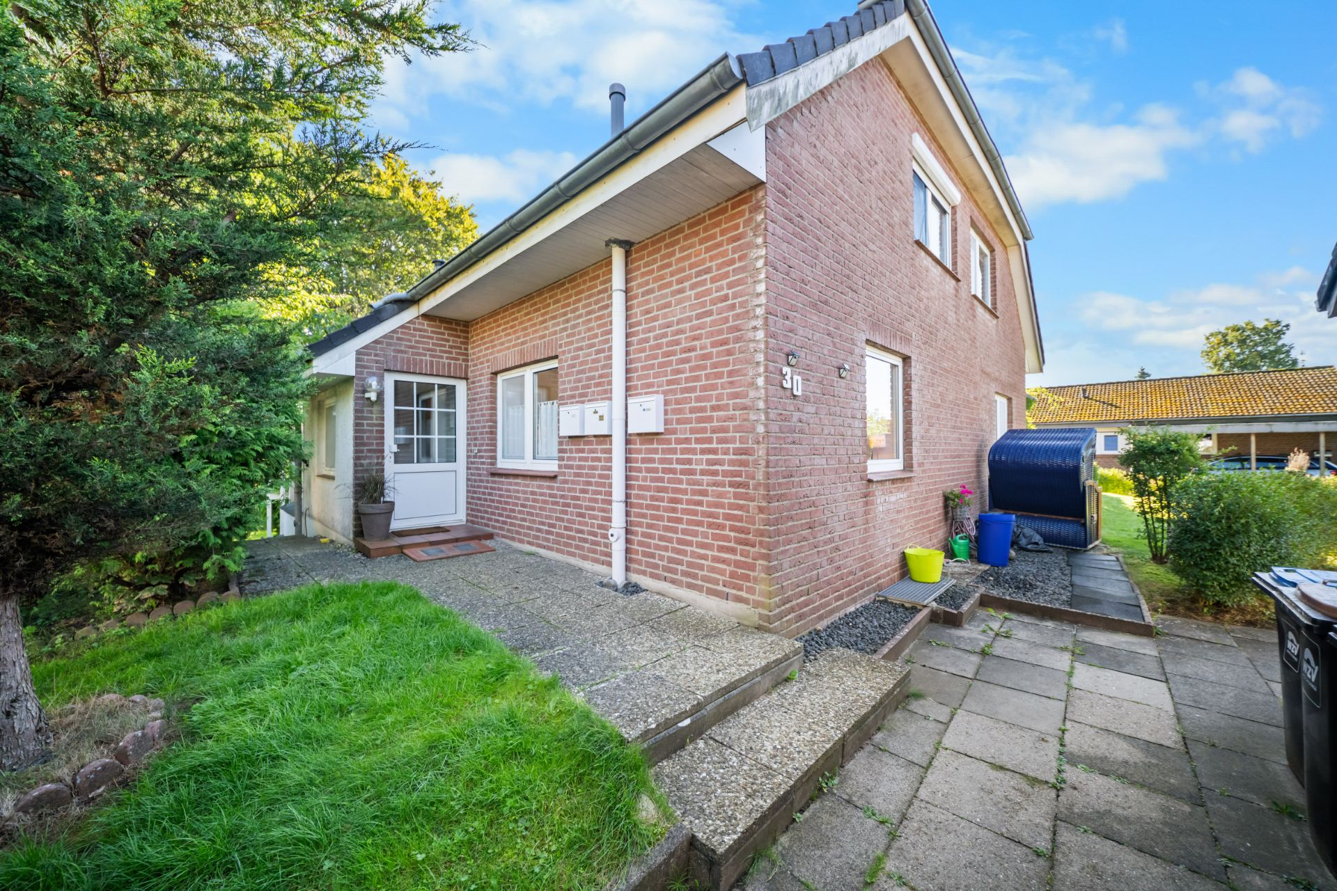 Backstein-Einfamilienhaus mit Terrasse, Garten, und angrenzendem Weg bei Tageslicht.