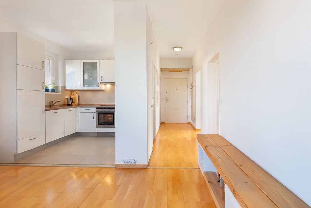 Heller Flur mit Holzbank und offener Küche mit weißen Schränken und Elektroherd.