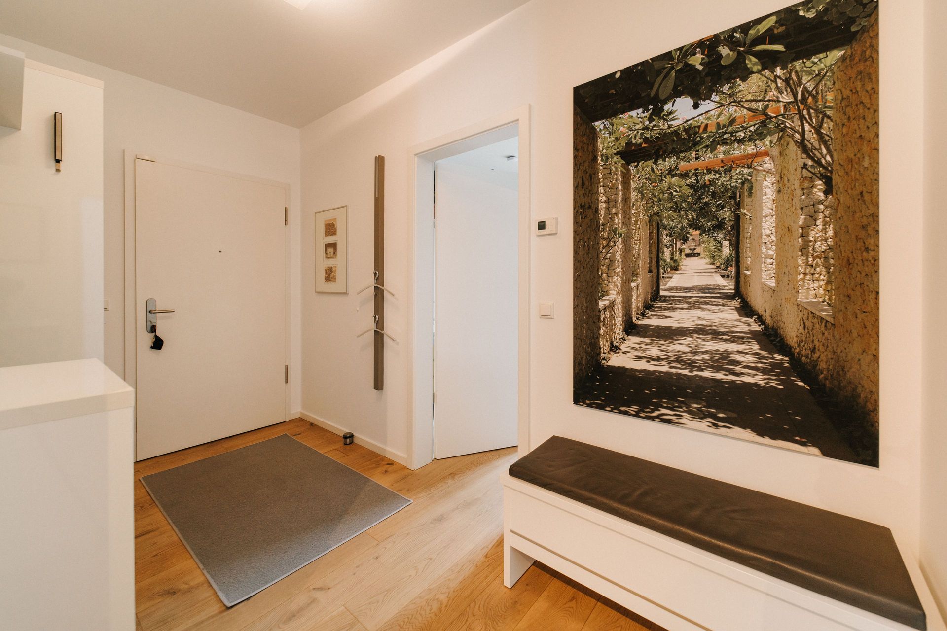 Heller Flur mit Holzboden, Bank, großem Bild und Türmatte vor der Wohnungstür.