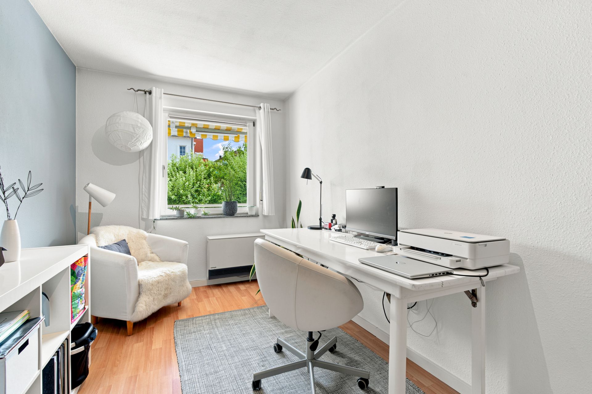 Helles Arbeitszimmer mit Schreibtisch, Bürostuhl, Sessel und Fenster mit Blick ins Grüne.