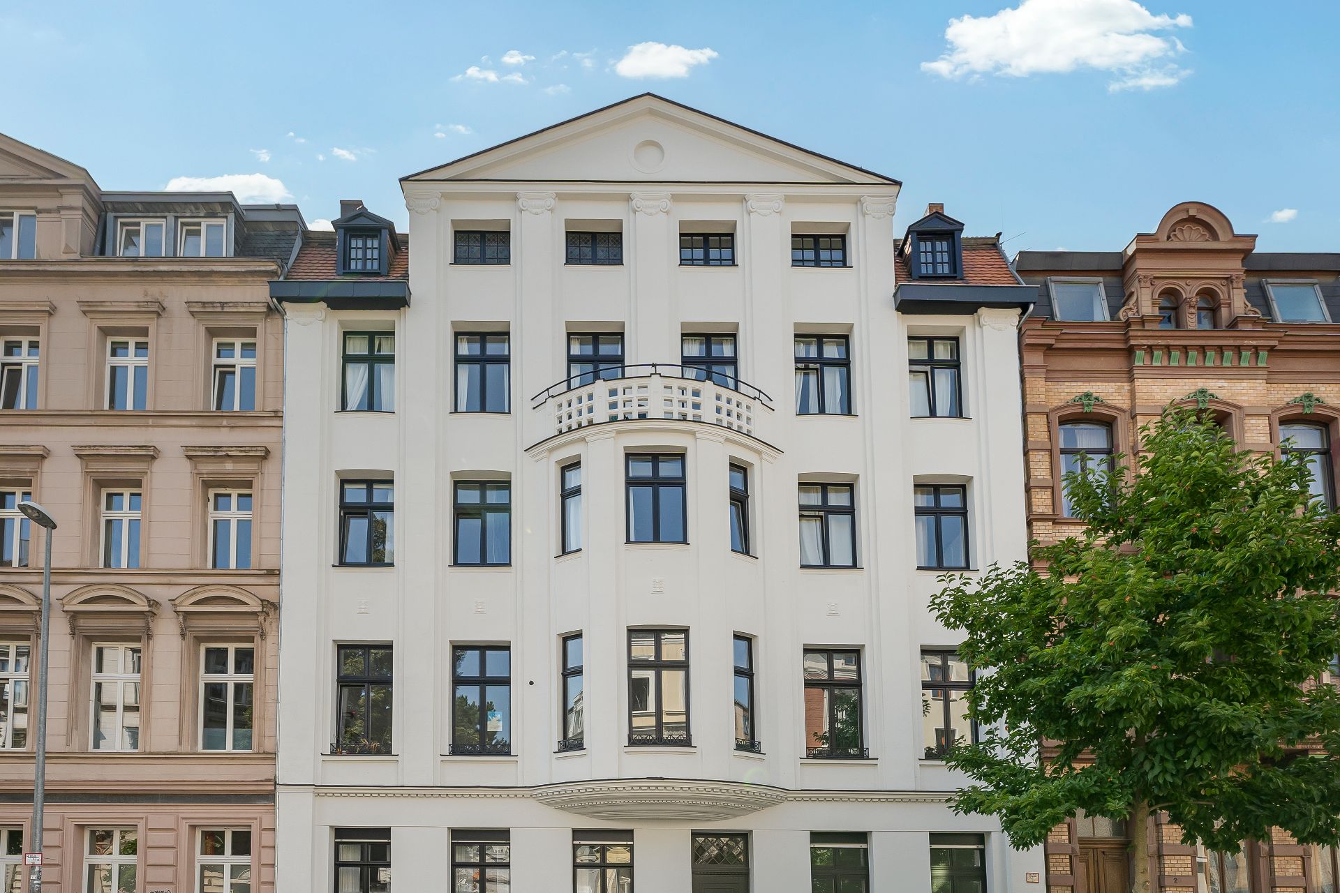 Fassade eines weißen Wohnhauses mit vielen Fenstern und einem kleinen Balkon.