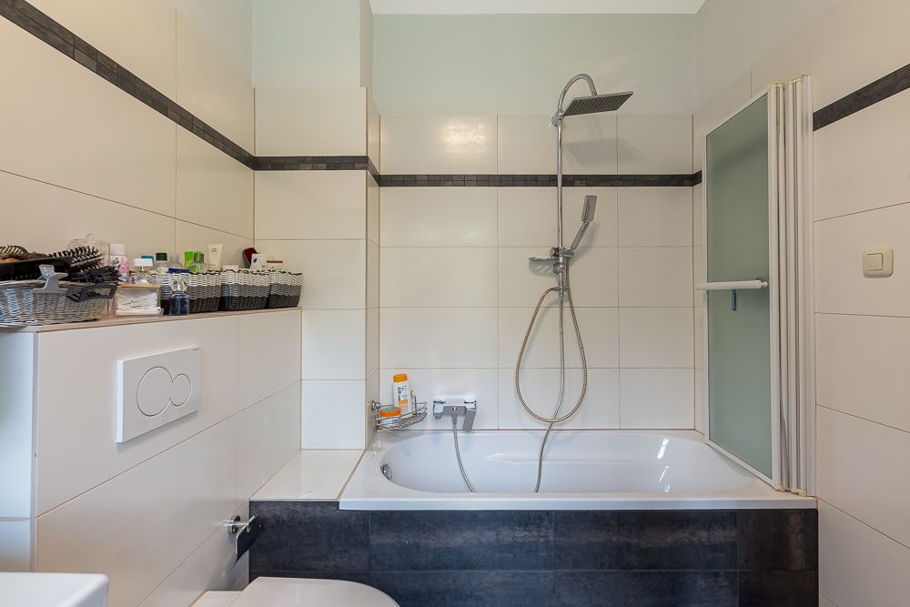 Badezimmer mit Badewanne, Duschkopf, Toilettenspülung und Ablage mit Pflegeprodukten.