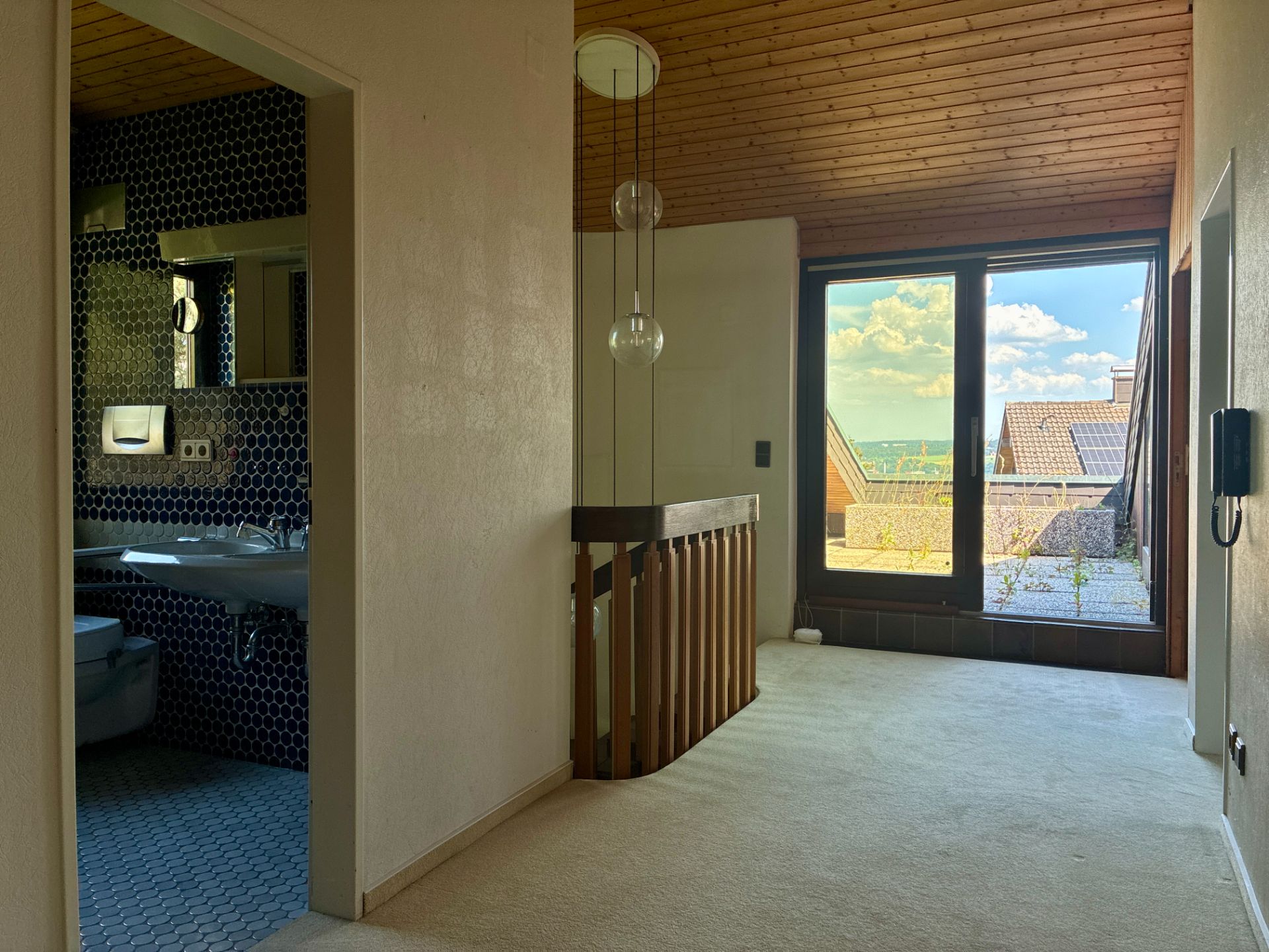 Flur mit Teppichboden, Treppengeländer, Zugang zum Badezimmer und Fenster mit Blick nach draußen.