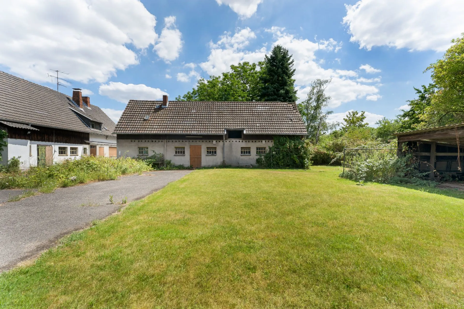 Großer Garten mit Rasen, Zufahrt und einem Wohnhaus im Hintergrund.