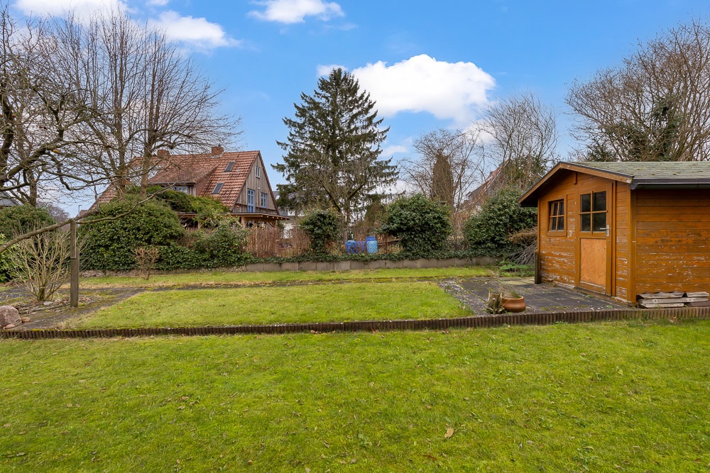 Garten mit Rasenfläche, Bäumen, Sträuchern und einem Holzschuppen rechts im Bild.