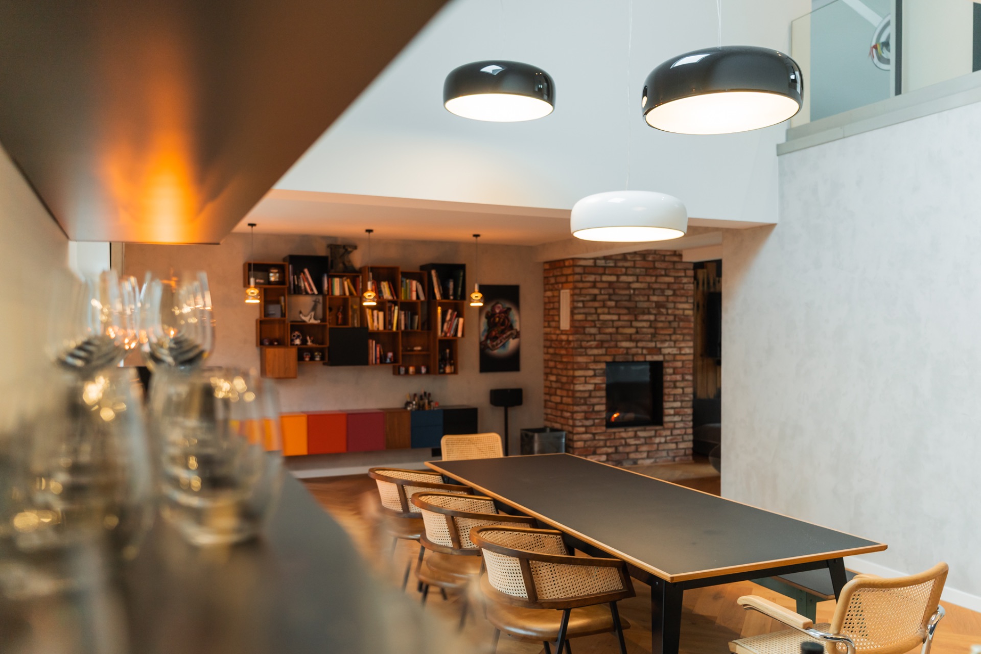 Modernes Esszimmer mit großem Tisch, Stühlen, Wandregalen und Kamin vor Backsteinwand.