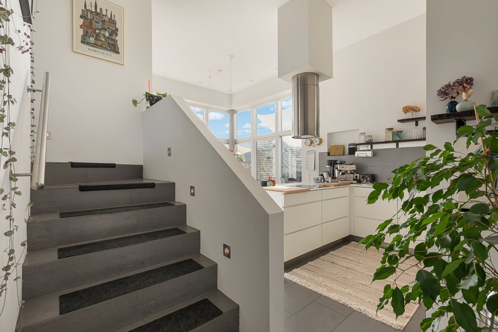 Helle moderne Küche mit großen Fenstern, Pflanzen und Treppe im Vordergrund.