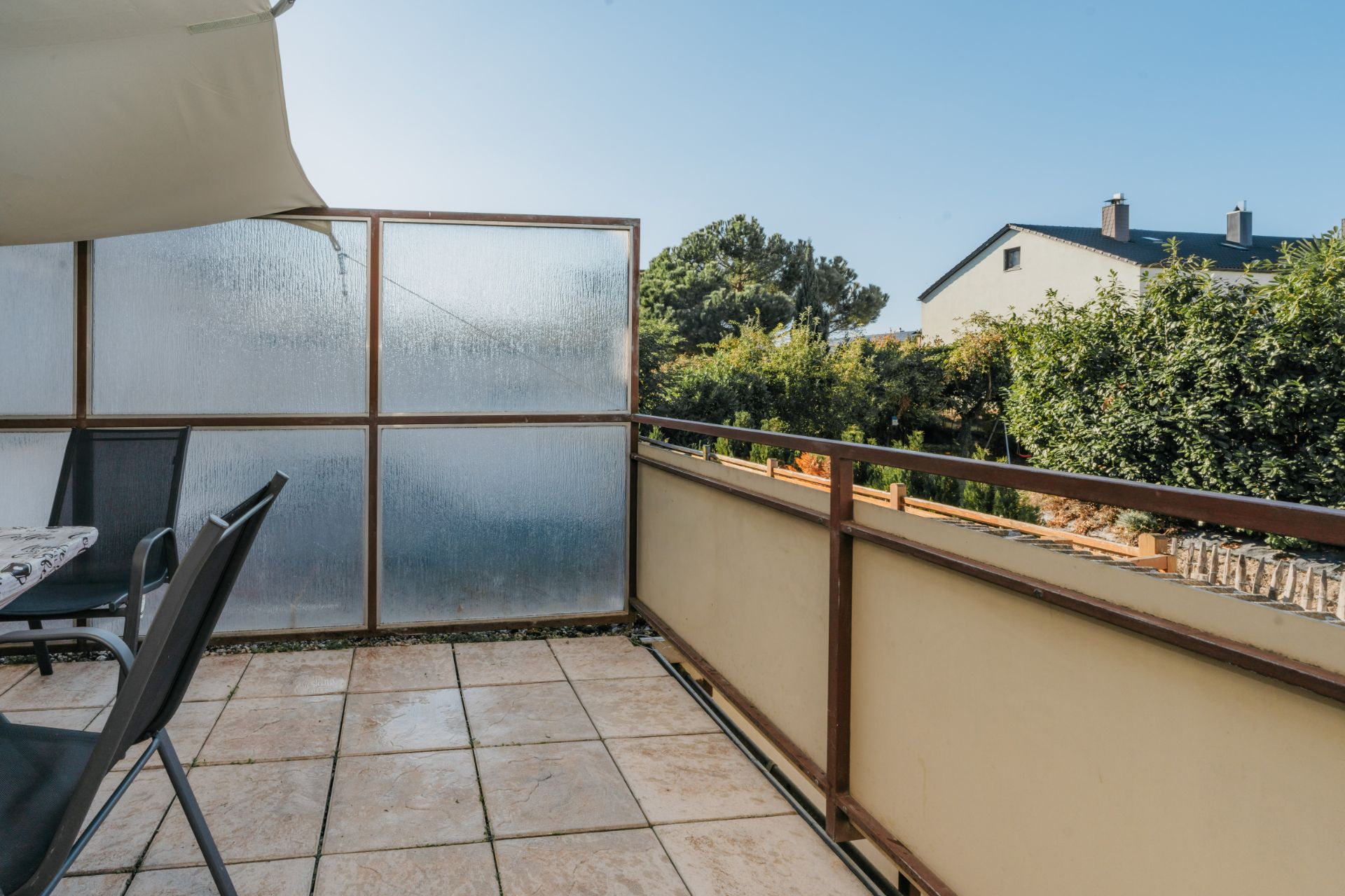 Balkon mit Fliesenboden, Sichtschutz und Blick auf Garten und Nachbarhaus.