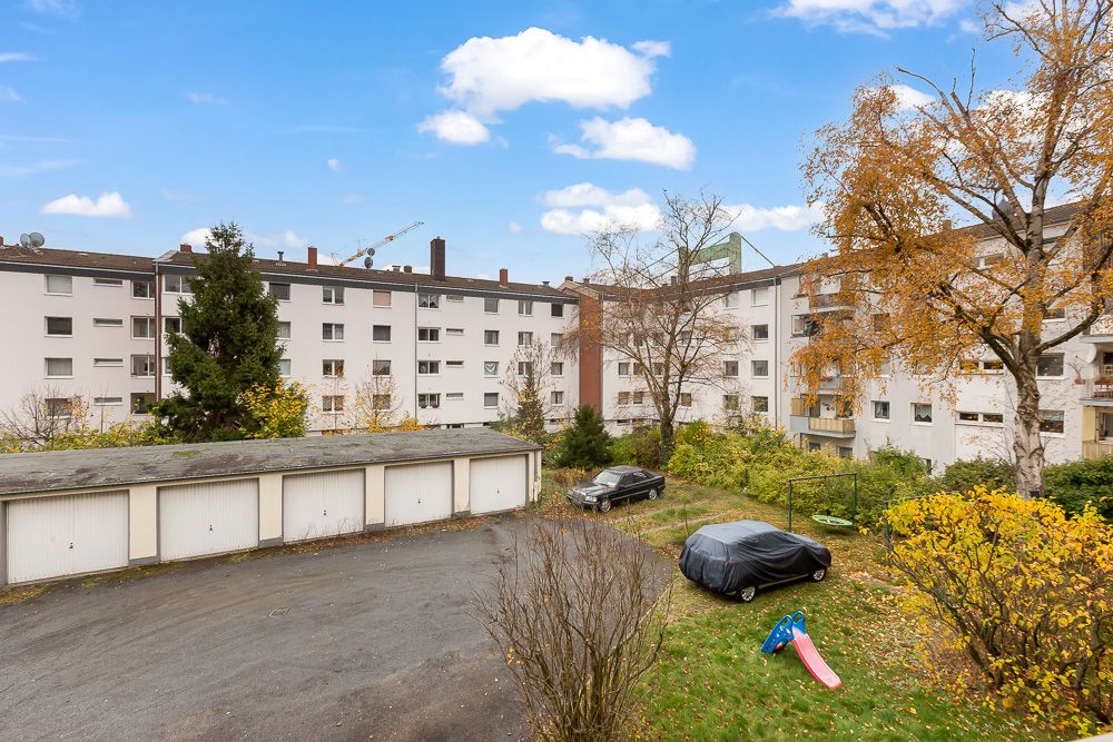 Mehrfamilienhäuser mit Garagenhof, geparkten Autos und Rutsche im begrünten Innenhof.