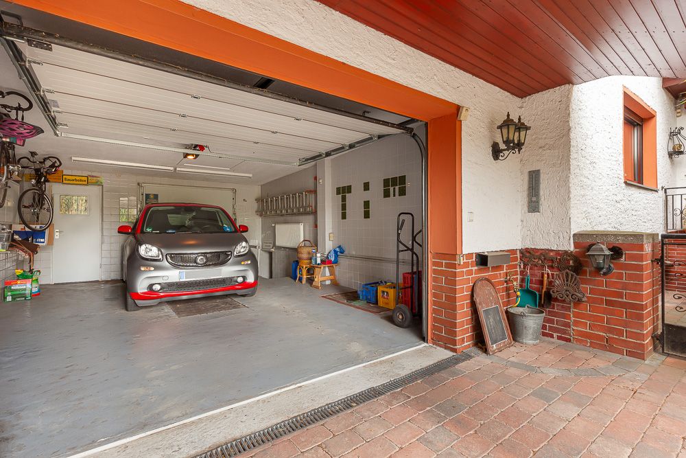 Offene Garage mit einem Auto, Fahrrädern und verschiedenen Haushaltsgegenständen an den Wänden.