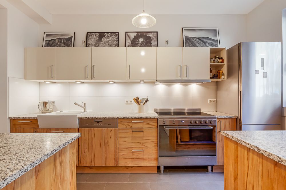 Moderne Küche mit Holzschränken, Spüle, Herd und großem Edelstahlkühlschrank.