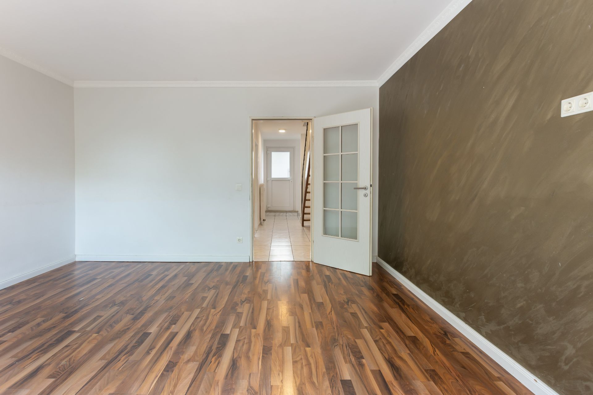 Leerer Raum mit Holzboden, weißer Wand und geöffneter Tür zum Flur.