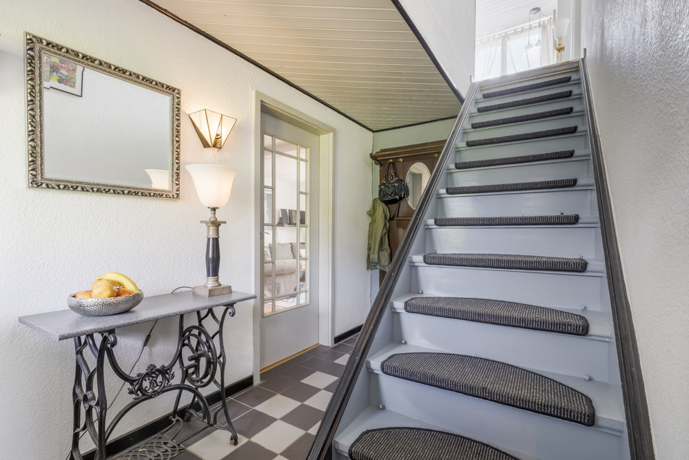 Flur mit Treppe, Spiegel, Tisch mit Obstschale und stehender Lampe an der Wand.