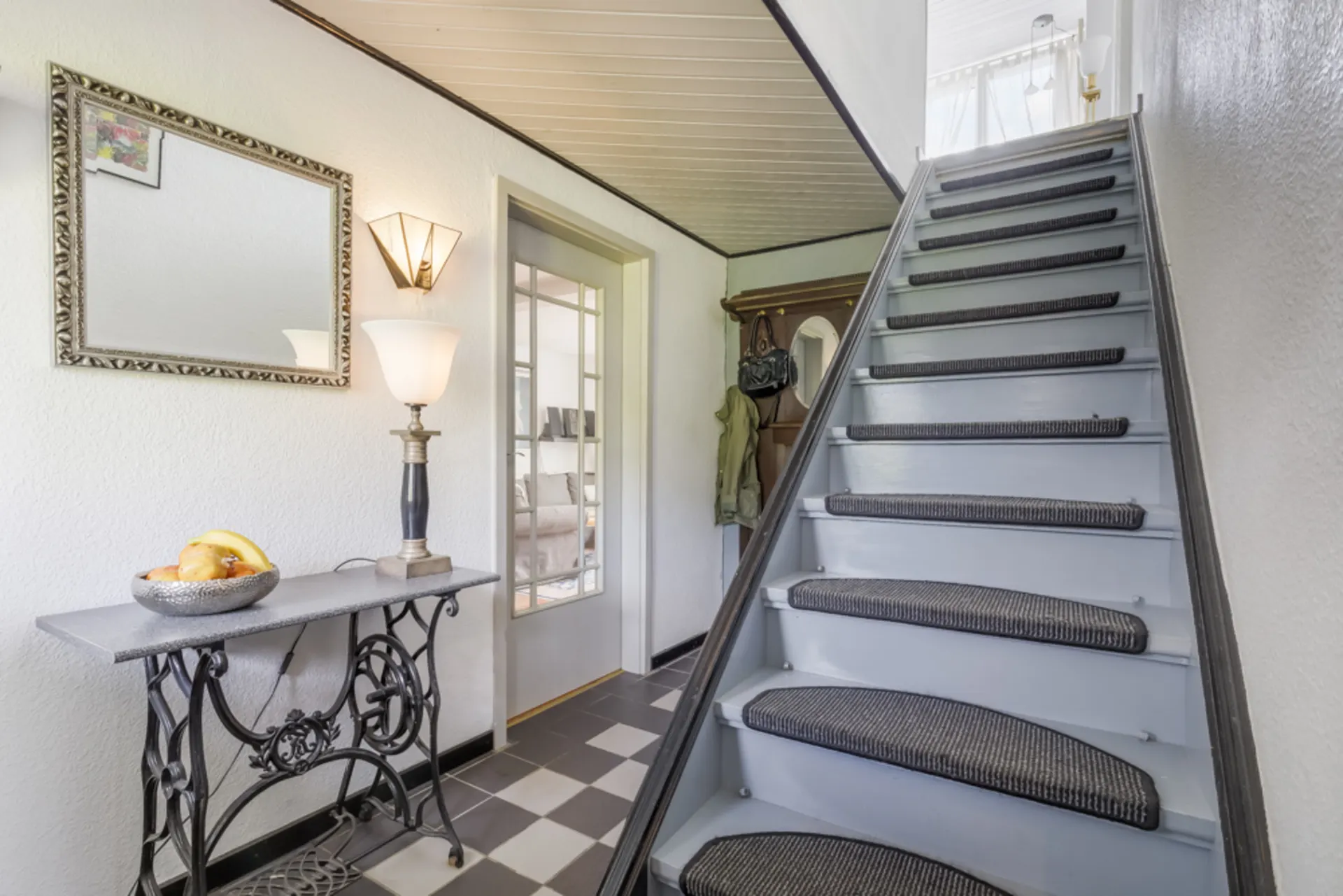 Flur mit Treppe, Spiegel, Tisch mit Obstschale und stehender Lampe an der Wand.