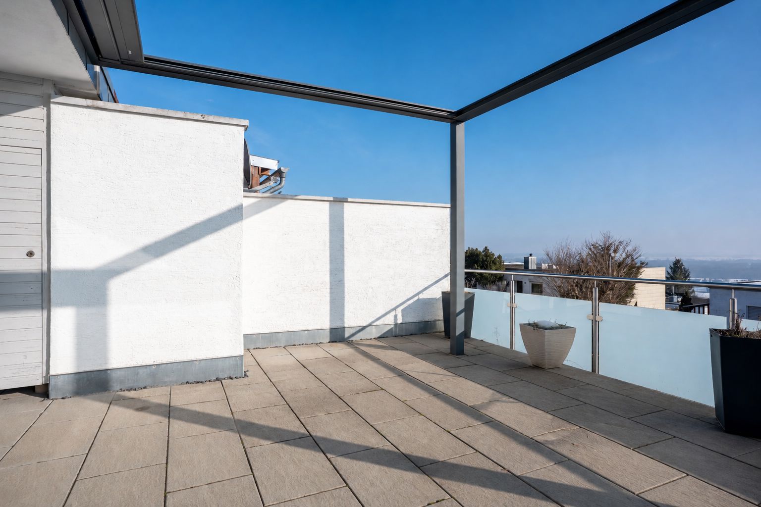 Große Dachterrasse mit Fliesenboden, Glasgeländer und zwei Pflanzkübeln, sonnig und mit Ausblick.