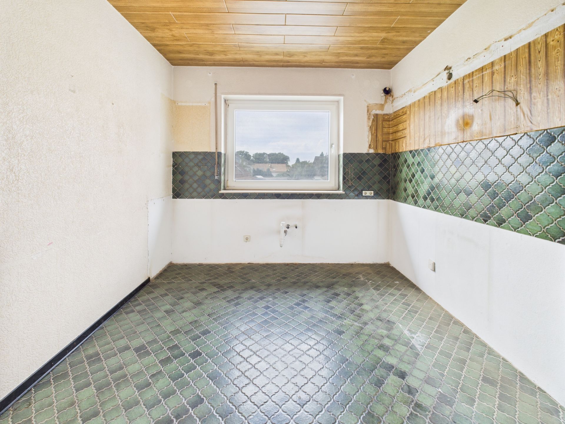 Leerer Raum mit grün gefliestem Boden, grünem Fliesenspiegel und Fenster an der Rückwand.