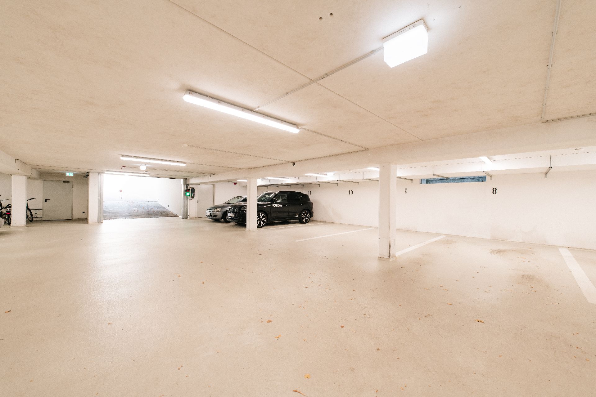 Helle Tiefgarage mit mehreren Parkplätzen, zwei Autos parken an der Wand.
