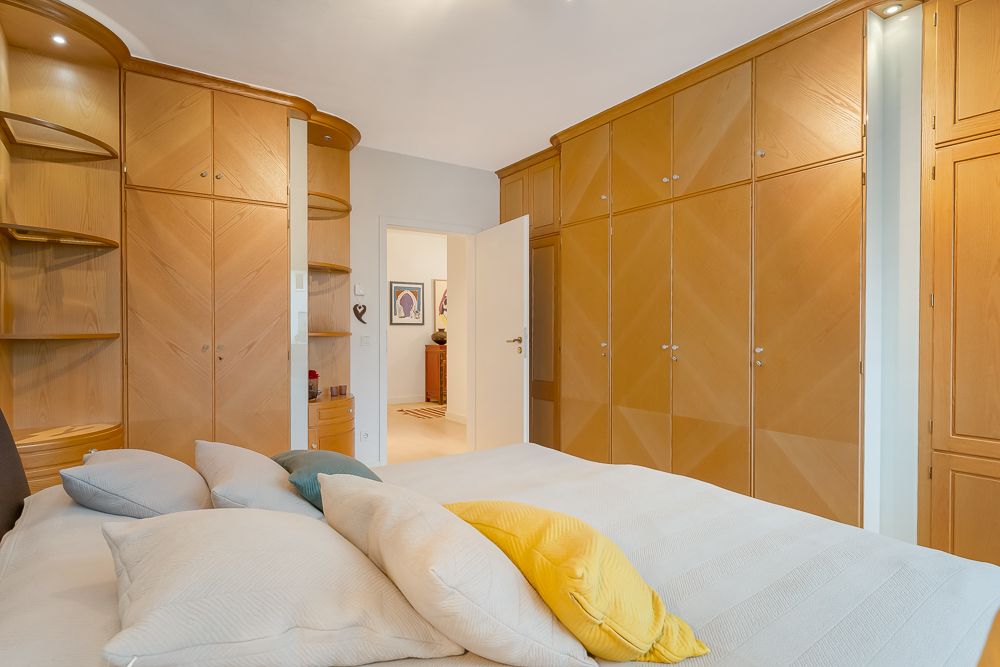 Schlafzimmer mit großem Bett, vielen Kissen und Einbauschränken aus Holz.