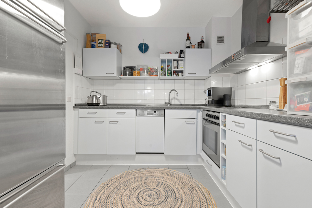Moderne Küche mit weißen Schränken, Rundteppich und Edelstahlgeräten.