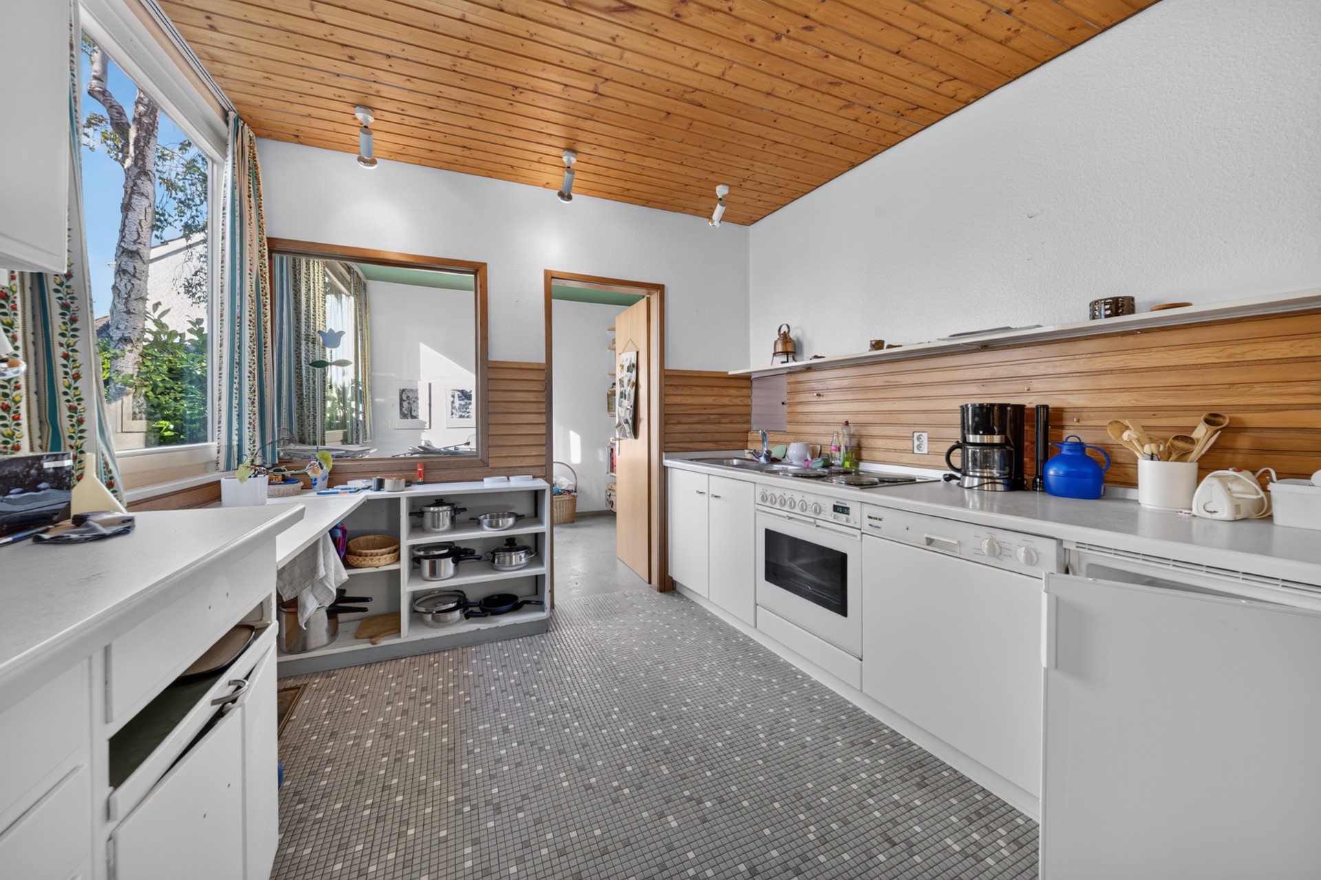 Helle Küche mit weißen Schränken, Holzwand und Decke, großem Fenster und offenem Regal.