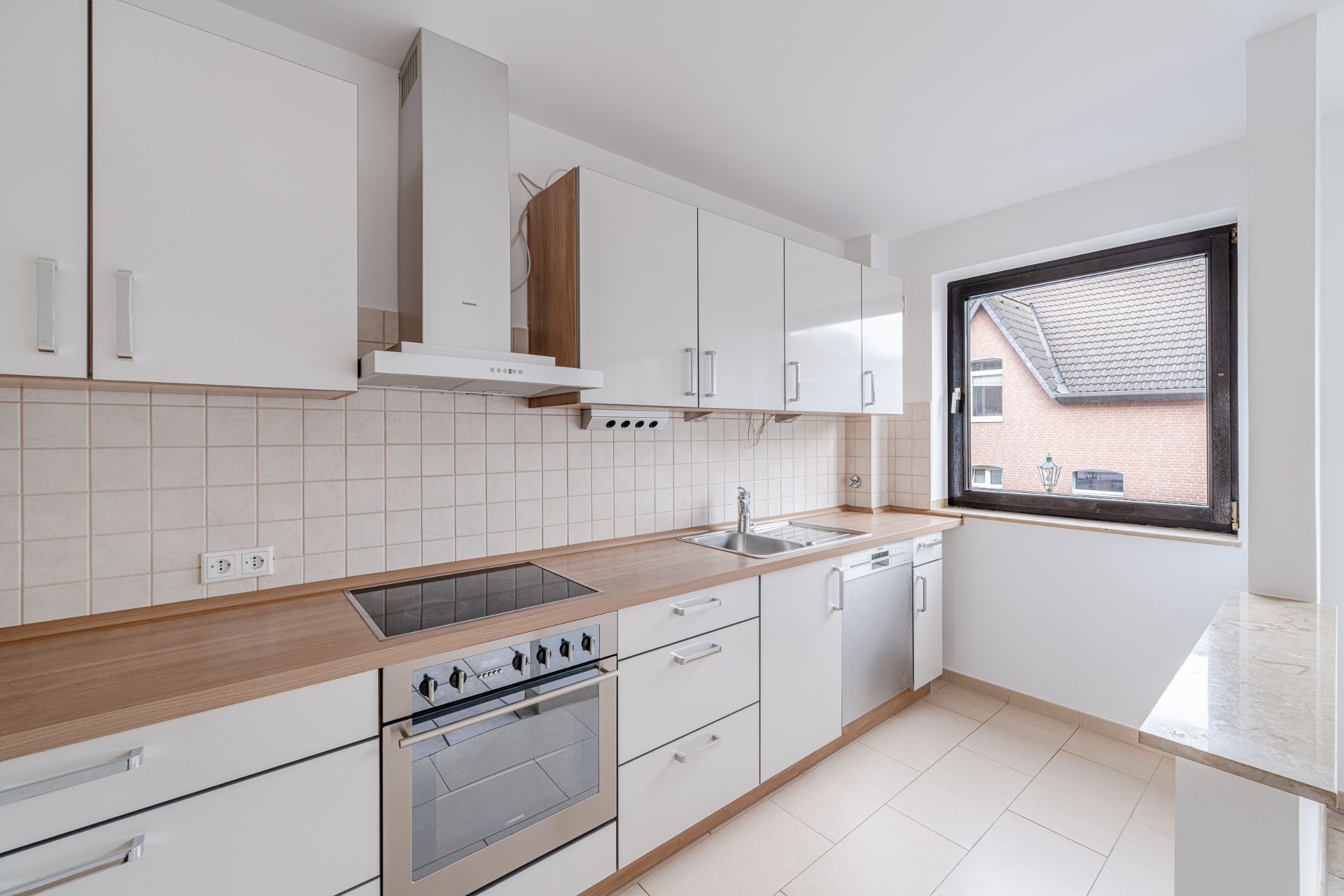 Moderne Einbauküche mit weißen Schränken, Herd, Spülmaschine und großem Fenster.