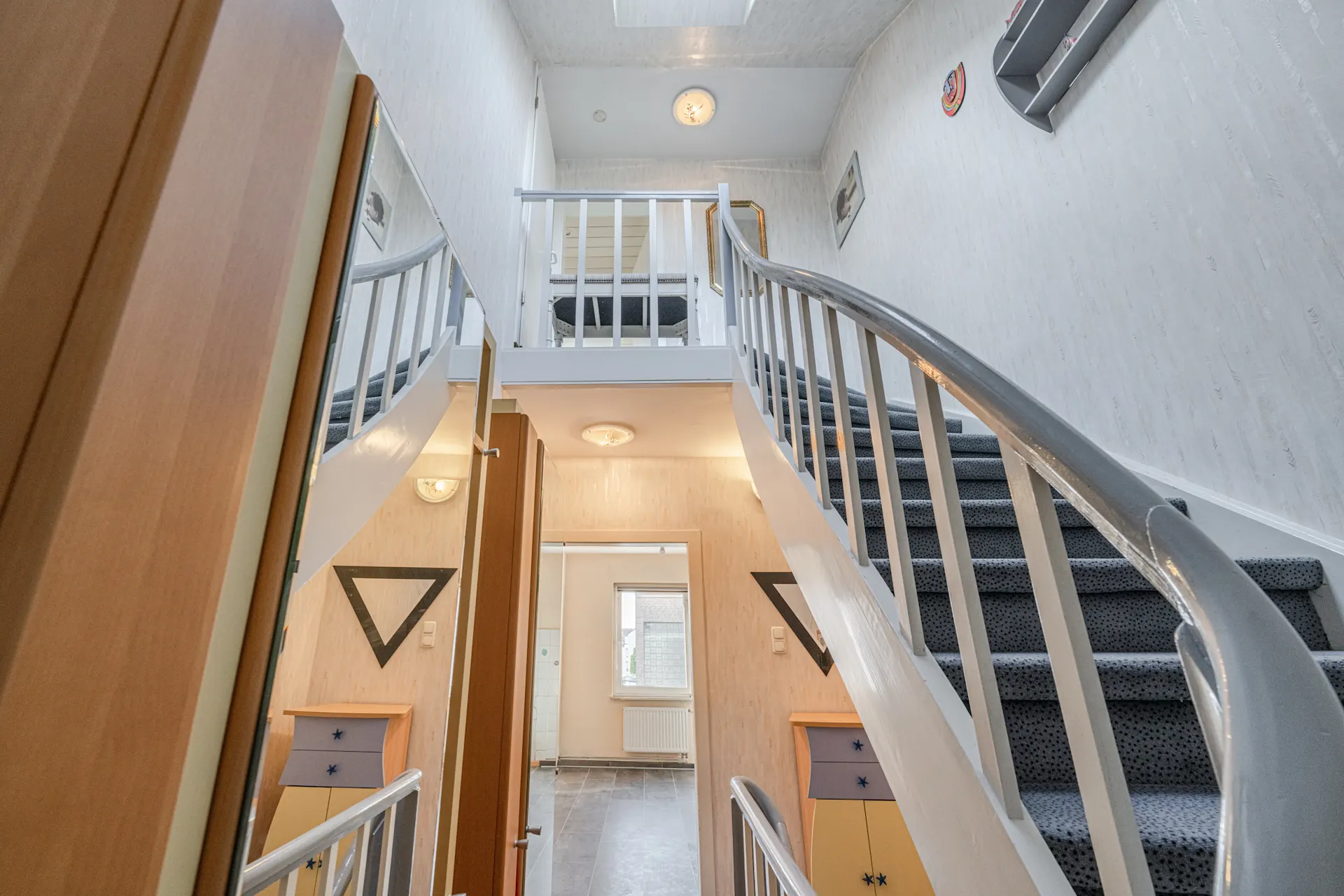 Heller Flur mit Teppichtreppe, weißen Geländern und Zugang zu oberen Etagen.