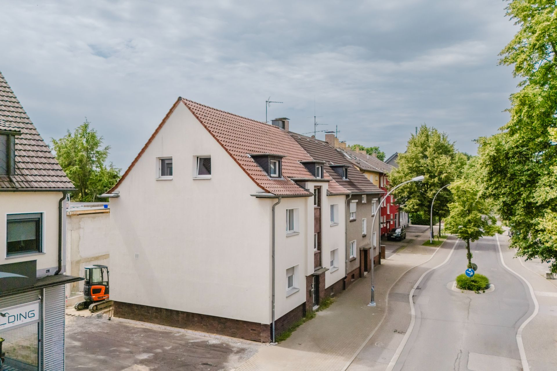 Mehrfamilienhaus mit Satteldach an einer ruhigen Straße mit Gehweg und Bäumen.