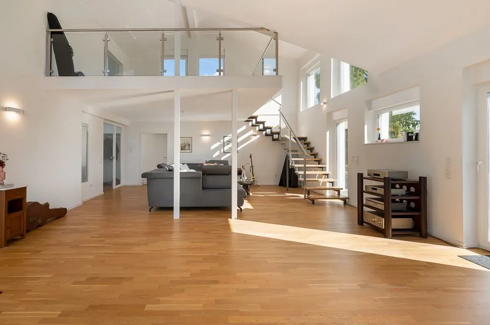 Helles Wohnzimmer mit Holzfußboden, grauem Sofa, offener Treppe und Galerie.