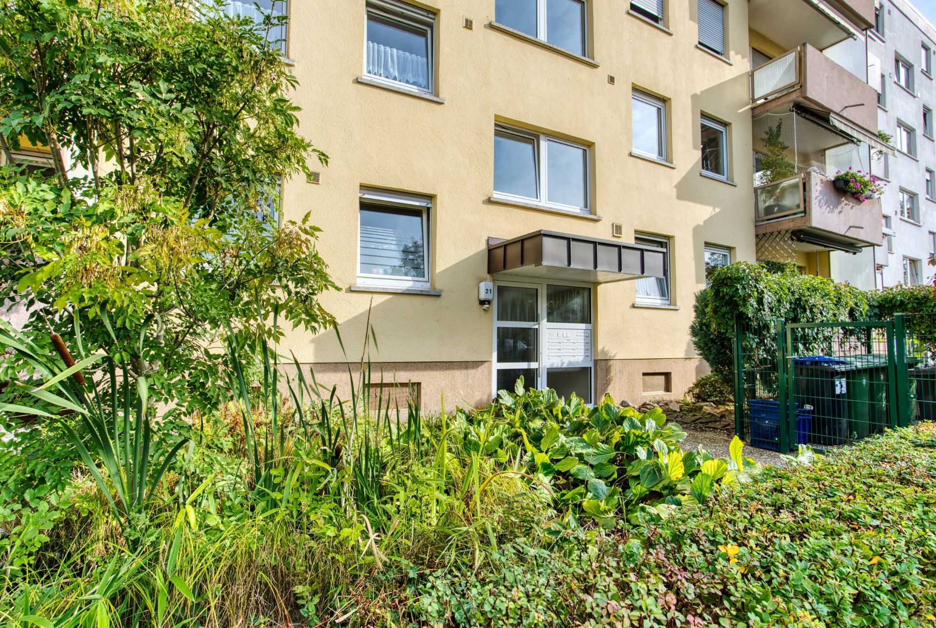 Eingang eines Mehrfamilienhauses mit Garten und mehreren Fenstern.