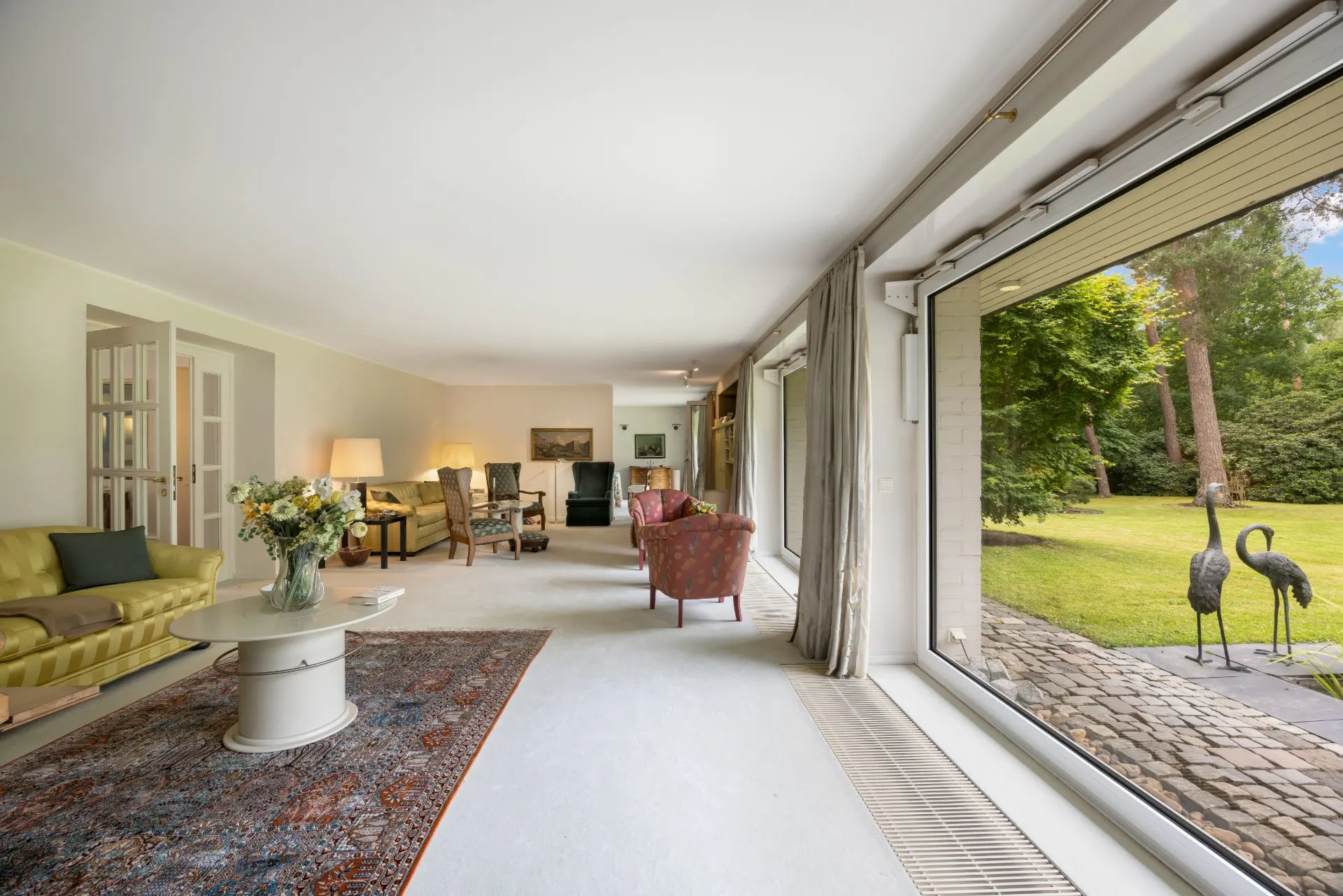 Helles Wohnzimmer mit Sofas, Sesseln und großem Fenster mit Blick auf den Garten.