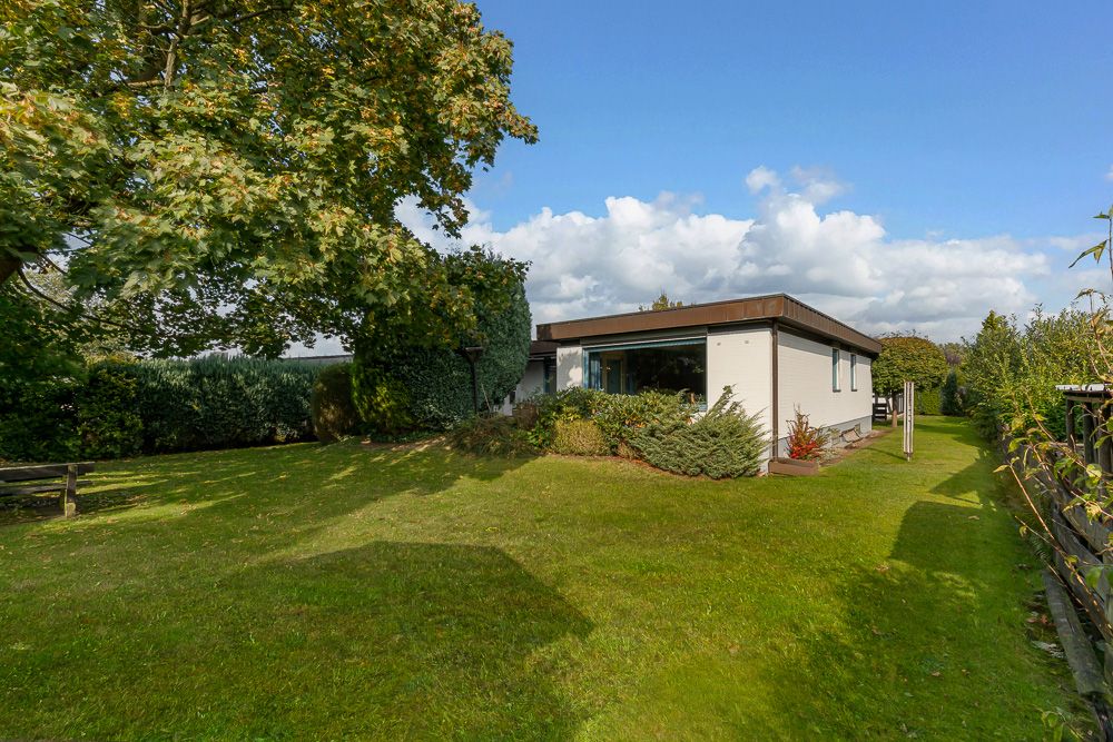 Einfamilienhaus mit Flachdach und großem Garten, umgeben von Bäumen und Hecken.