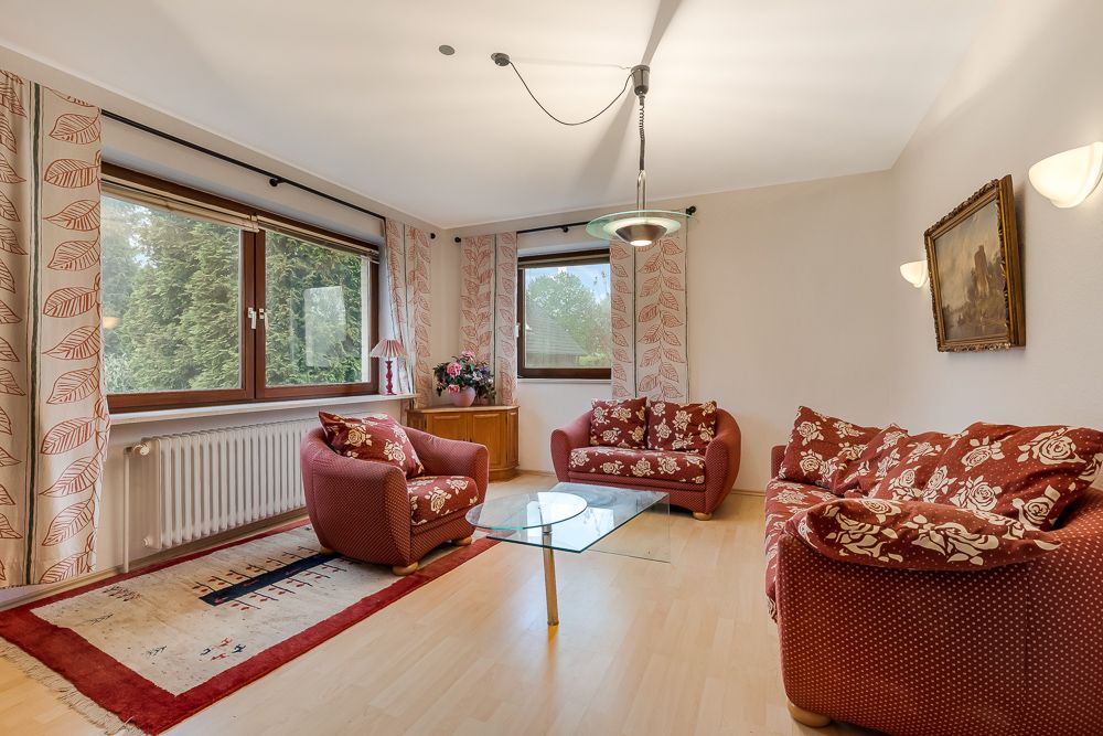 Wohnzimmer mit drei roten Sofas, Glastisch, Teppich, großen Fenstern und Wandbild.