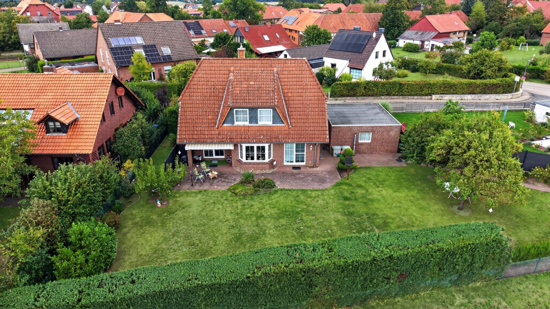 Luftaufnahme eines Einfamilienhauses mit rotem Dach und großem Garten, umgeben von Hecken.