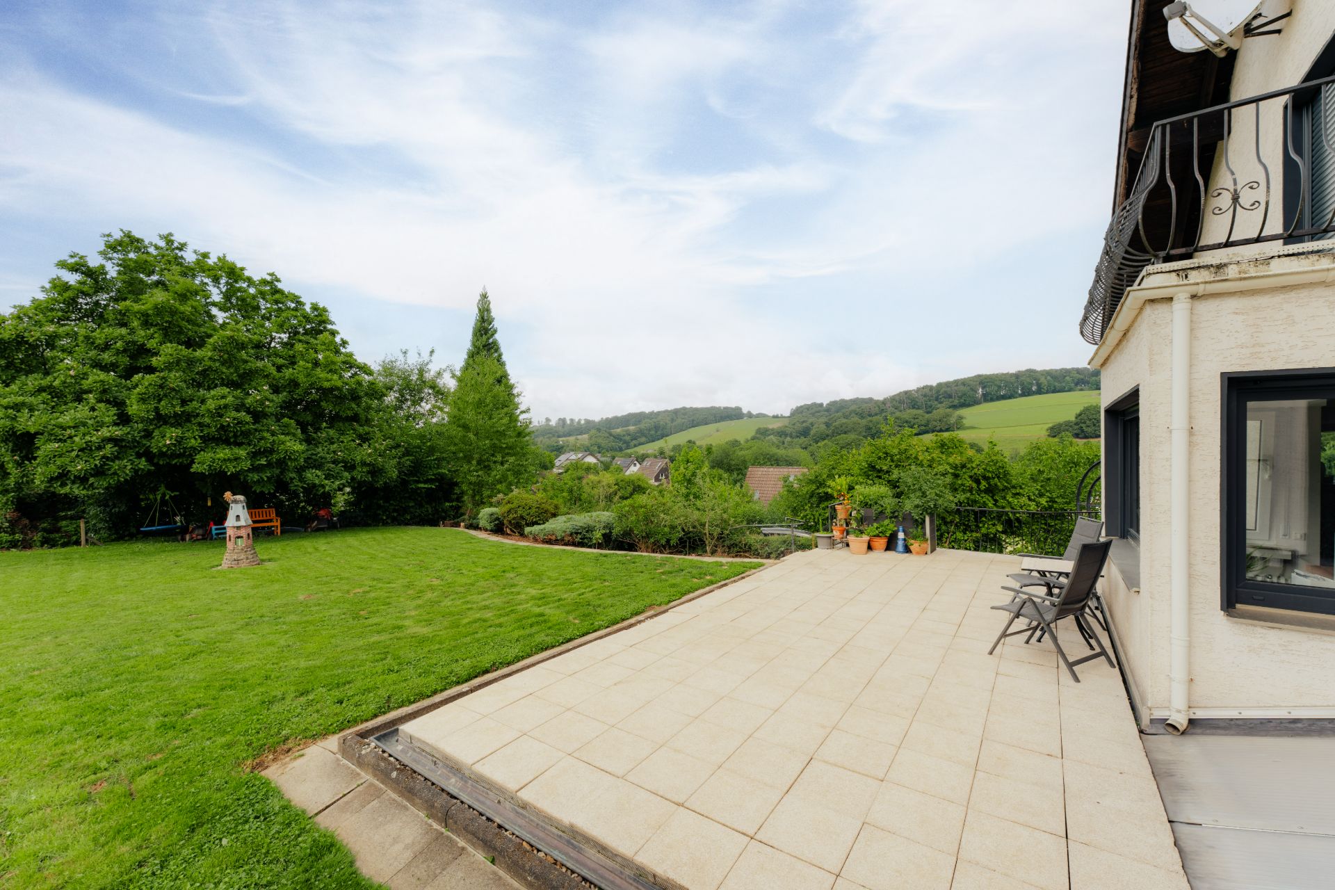 Große Terrasse mit Garten, Rasenfläche und Blick auf Hügel im Hintergrund.